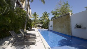 A swimming pool with lounge chairs and palm trees. - Downtown Apartment Oasis 12 (Playa del Carmen)