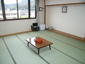 Una habitación con suelo de tatami, una mesa de madera con un recipiente naranja, un televisor y un mueble blanco pequeño.