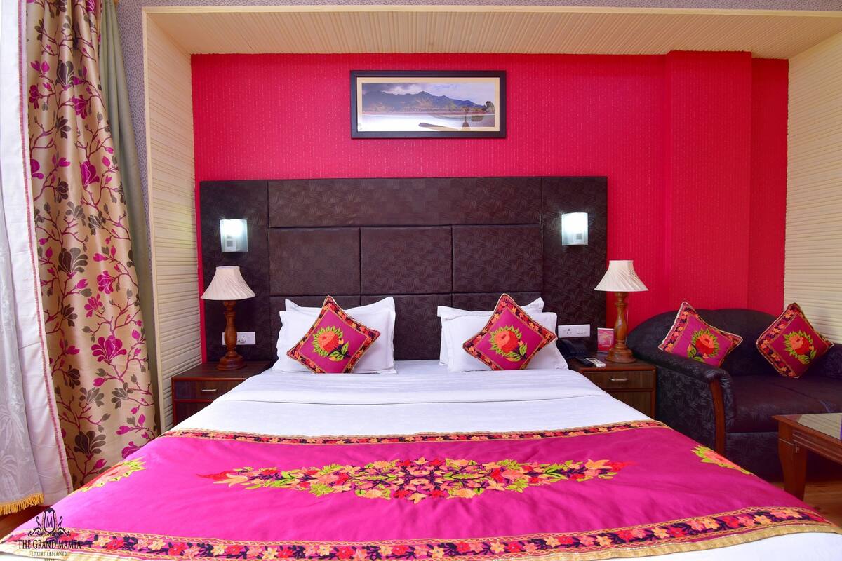 A hotel room with a large bed, two bedside tables with lamps, a dark headboard, and a red accent wall.