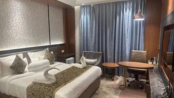 A hotel room with a large bed, a small table, a chair, and a desk with a chair.