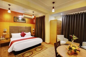 A hotel room with a large bed, a desk with a chair, a dining table with a vase of flowers, and a wardrobe. - Hotel The Grand Mamta (Srinagar)