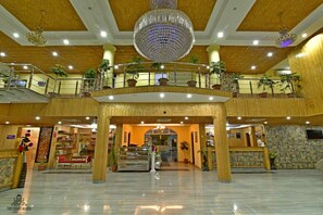 A spacious lobby with a grand chandelier, multiple levels with balconies, and potted plants. - Hotel The Grand Mamta (Srinagar)