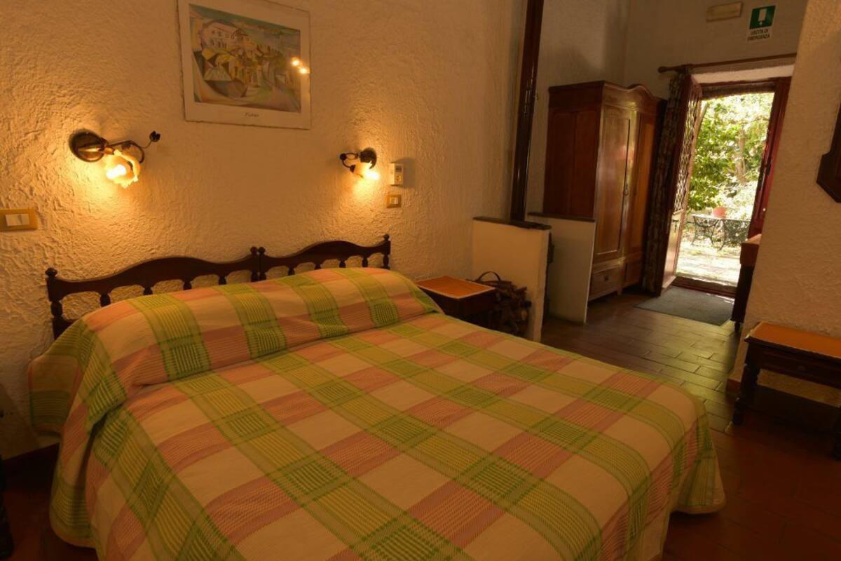 A bedroom with a bed, two wall-mounted lamps, a painting, and a door leading to a balcony.