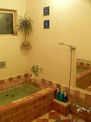 Un baño con bañera, ducha y lavamanos. Hay azulejos decorativos en las paredes y una planta en maceta.