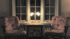 Una habitación con dos sillones tapizados, una mesa y un ventanal con lámpara.