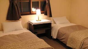 Habitación doble con dos camas, una mesita de noche, una lámpara y un ventanal con cortinas.
