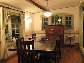 A dining room with a wooden table, chairs, a chandelier, and a window with curtains. - Country Inn Mori No Gorilla (Kitashiobara)