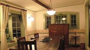 Un comedor con una mesa de madera, sillas, una lámpara de araña y un ventanal con cortinas.