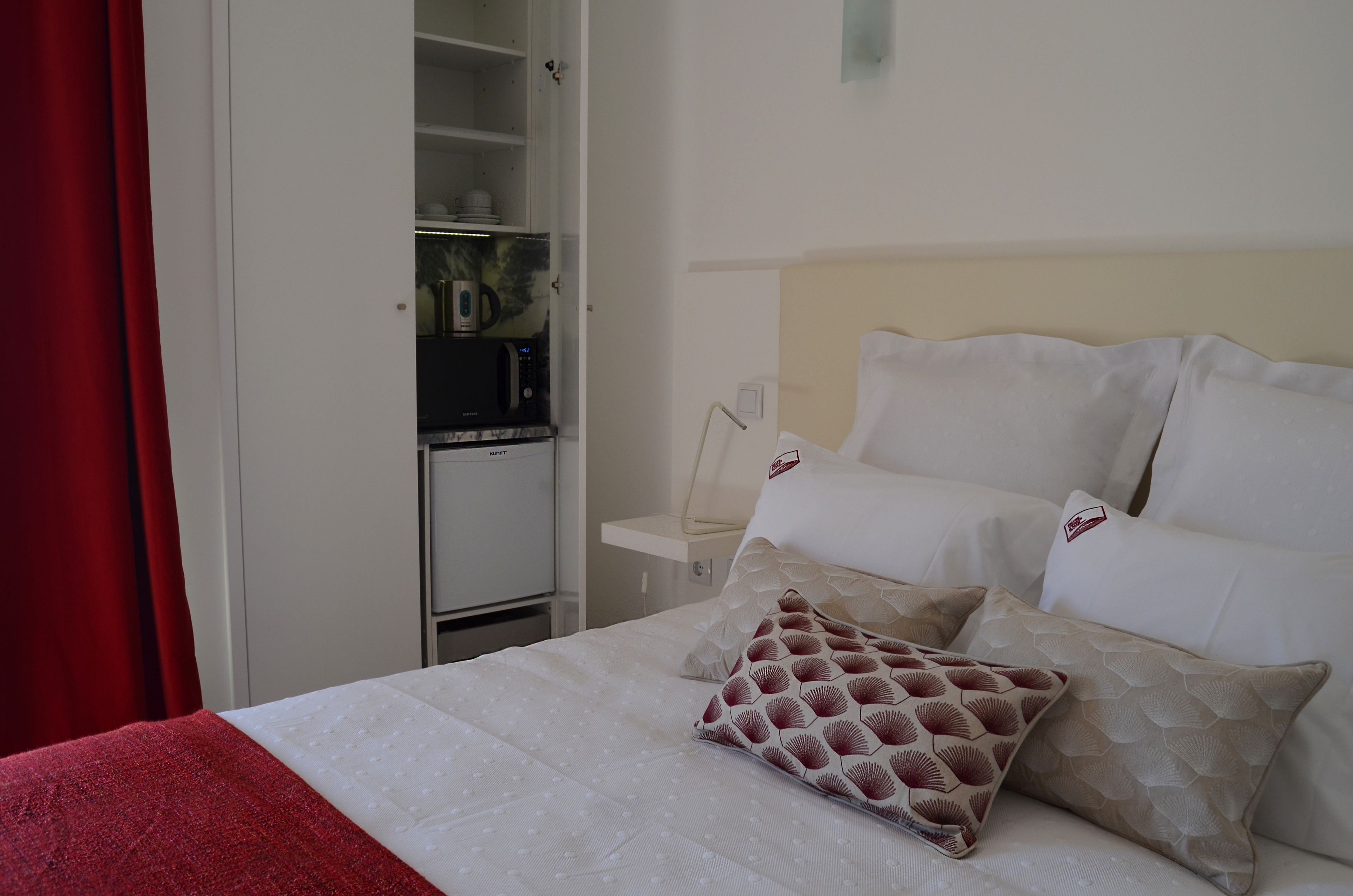 Una habitación de hotel con una cama, una mesita de noche, un armario blanco y una cortina roja.
