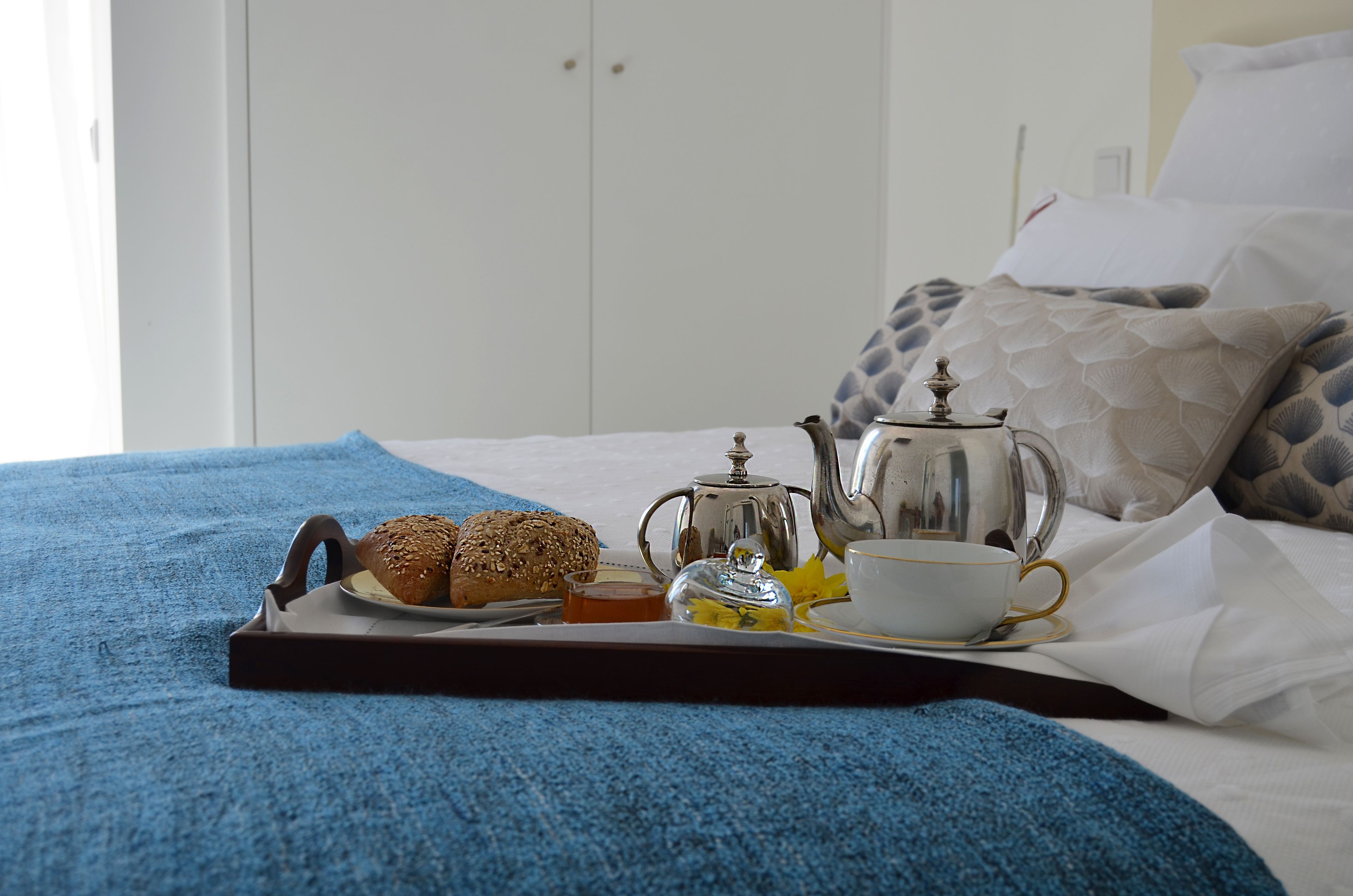 A neatly made bed with a tray of breakfast items including bread, tea, and a cup.
