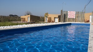 Una piscina con agua azul cristalina, rodeada por una cerca de madera y un pequeño edificio con una puerta.