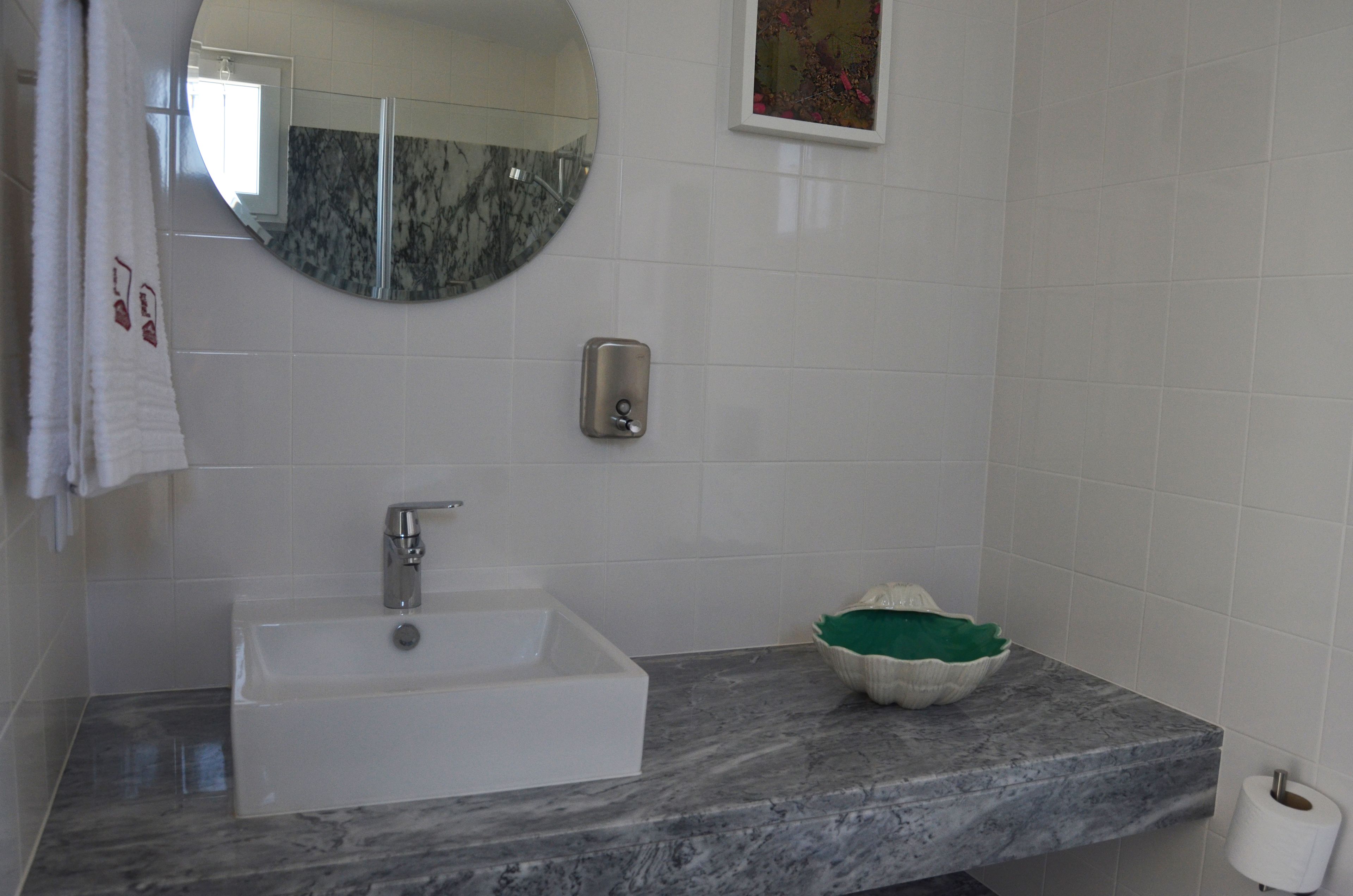 A bathroom with a white sink, a mirror, a soap dispenser, and a decorative bowl on the countertop.