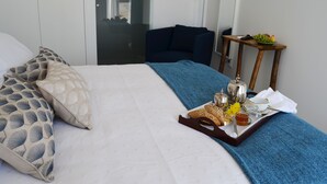 Una cama bien hecha con una bandeja de desayuno, que incluye pan, té y fruta, en una habitación de hotel moderna con vistas al exterior.