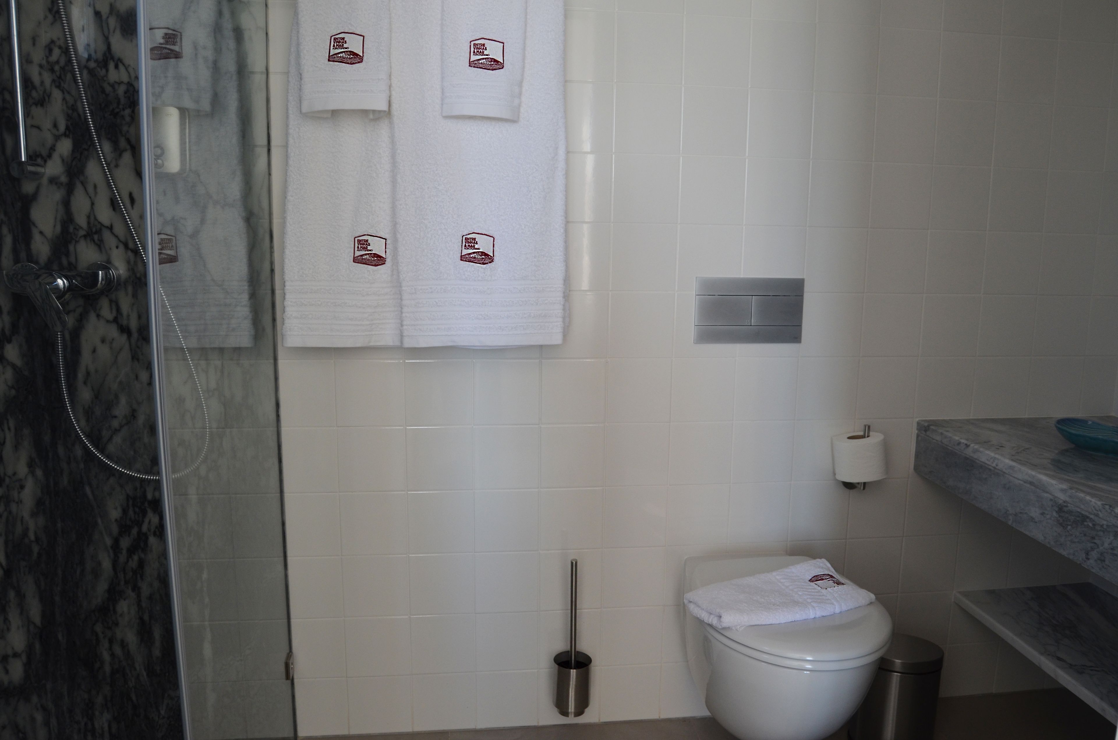 A bathroom with a shower, toilet, and marble-tiled walls.