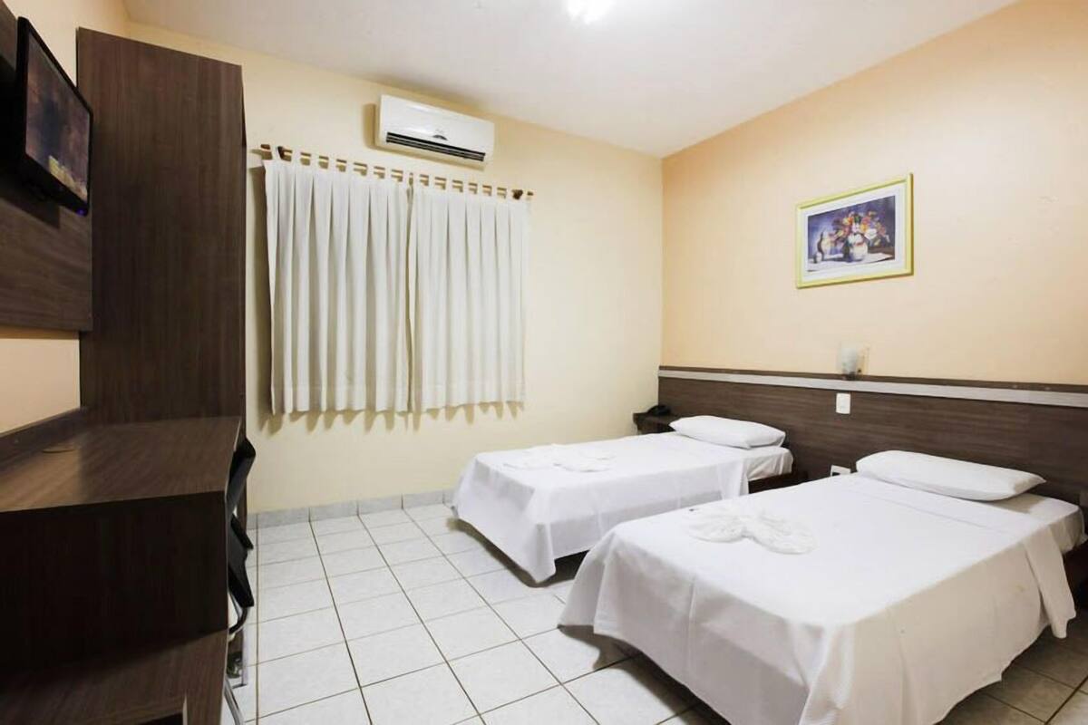 Ett hotellrum med två sängar, ett skrivbord, en luftkonditionering och en tavla på väggen.