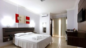 Habitación de hotel con cama, escritorio, televisor y baño visible a través de una puerta abierta.