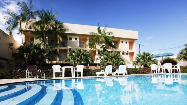Una piscina con azulejos azules, rodeada de sillas reclinables blancas y palmeras.