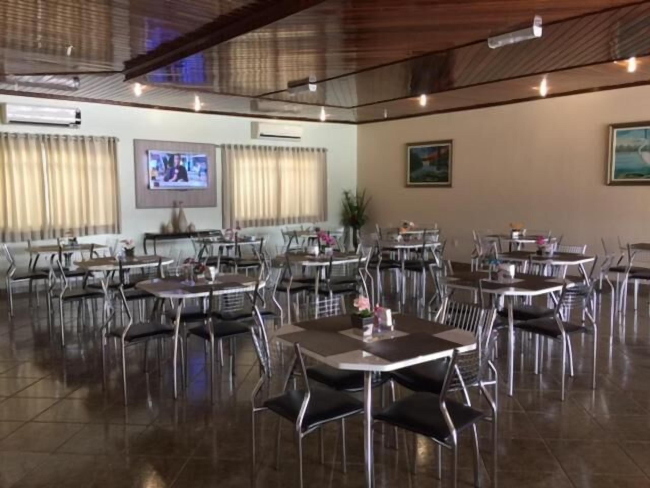 A spacious dining area with multiple tables and chairs, air conditioning units, and a television screen on the wall.