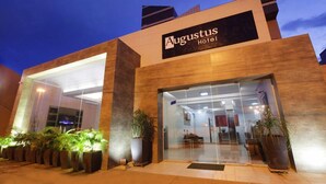 Exterior del Hotel Augustus, con un diseño moderno, que presenta grandes puertas de vidrio y plantas en macetas.