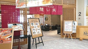 Een restaurant interieur met een traditionele Japanse uitstraling, met tatami vloeren en shoji schermen. Er staan menukaarten op schragen en een bord met Japanse tekens.