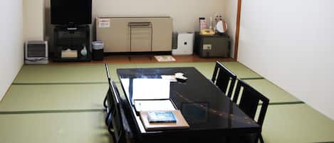 A tatami mat room with a black table, chairs, a television, a heater, and a small cabinet with a mirror and other items.