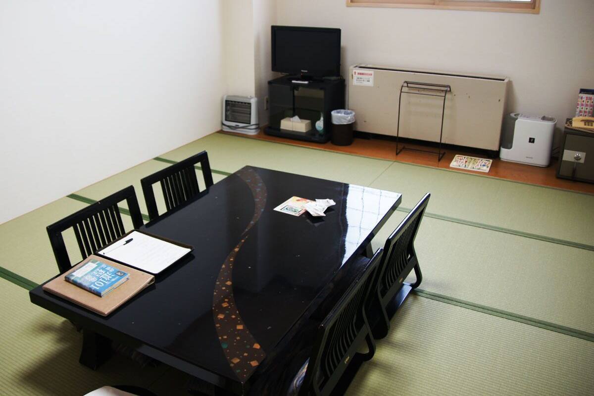 A room with tatami flooring, a black table with chairs, a television, a heater, and a small cabinet.