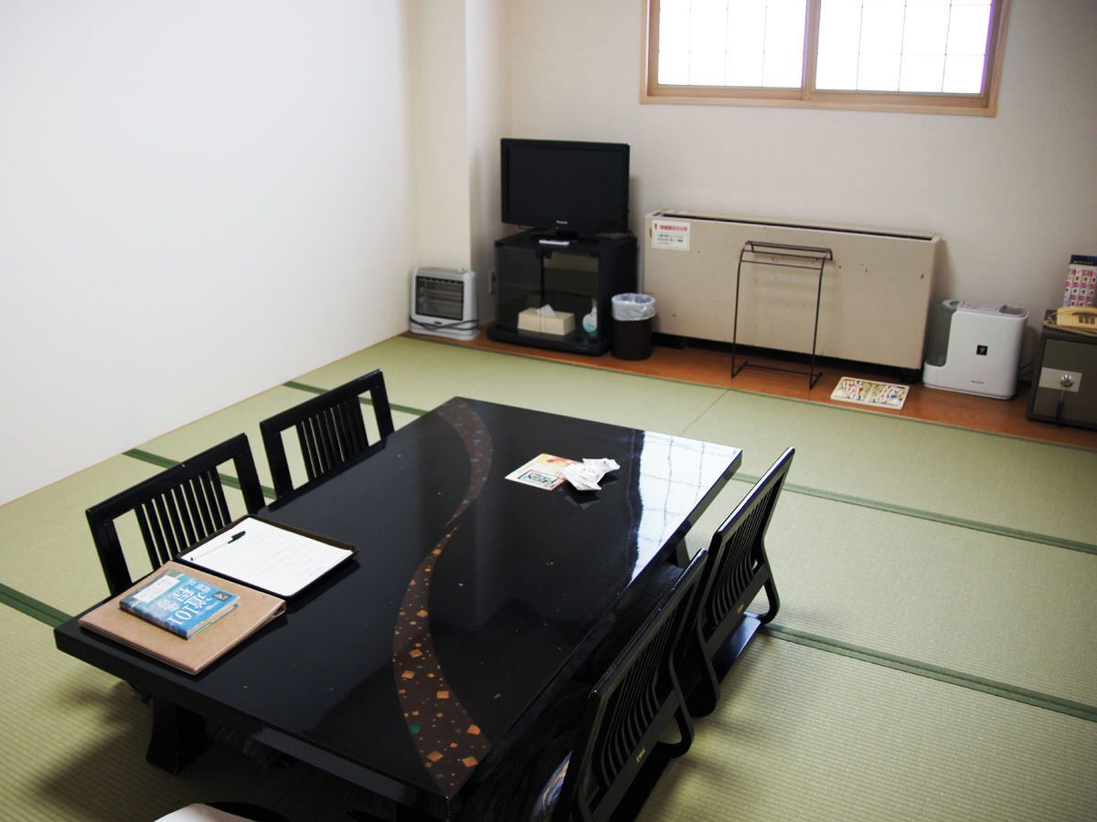 A room with tatami flooring, a black table with chairs, a television, a small heater, and a cabinet.