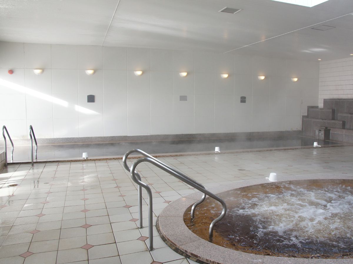 A steam room with a hot tub, tiled floor, and metal handrails.