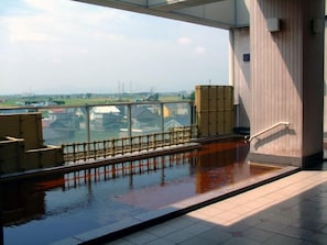 A view from a high floor with a pool, a wooden deck, and a railing overlooking a body of water and distant buildings.