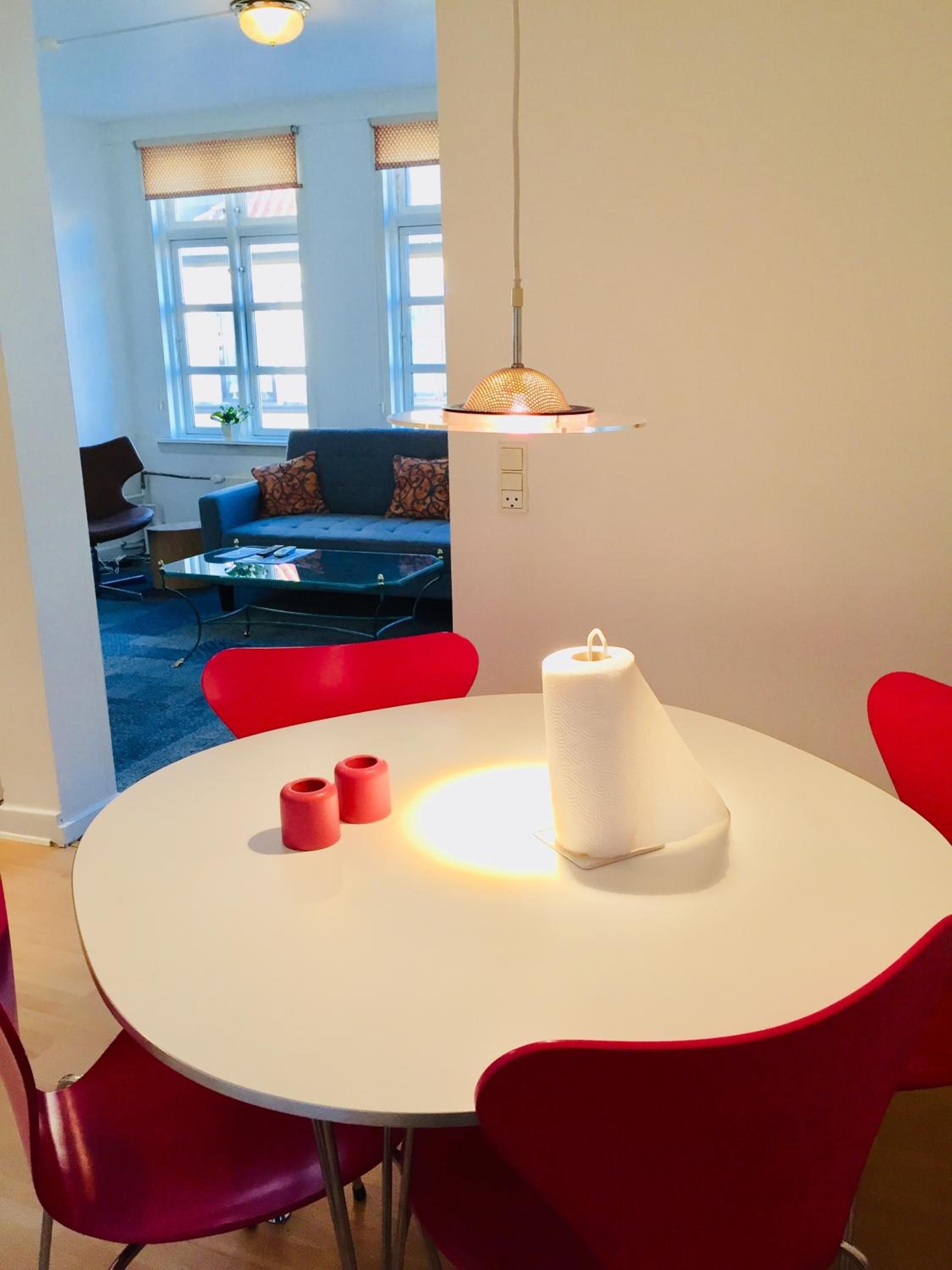 Un comedor con una mesa redonda, sillas rojas y una vela blanca.