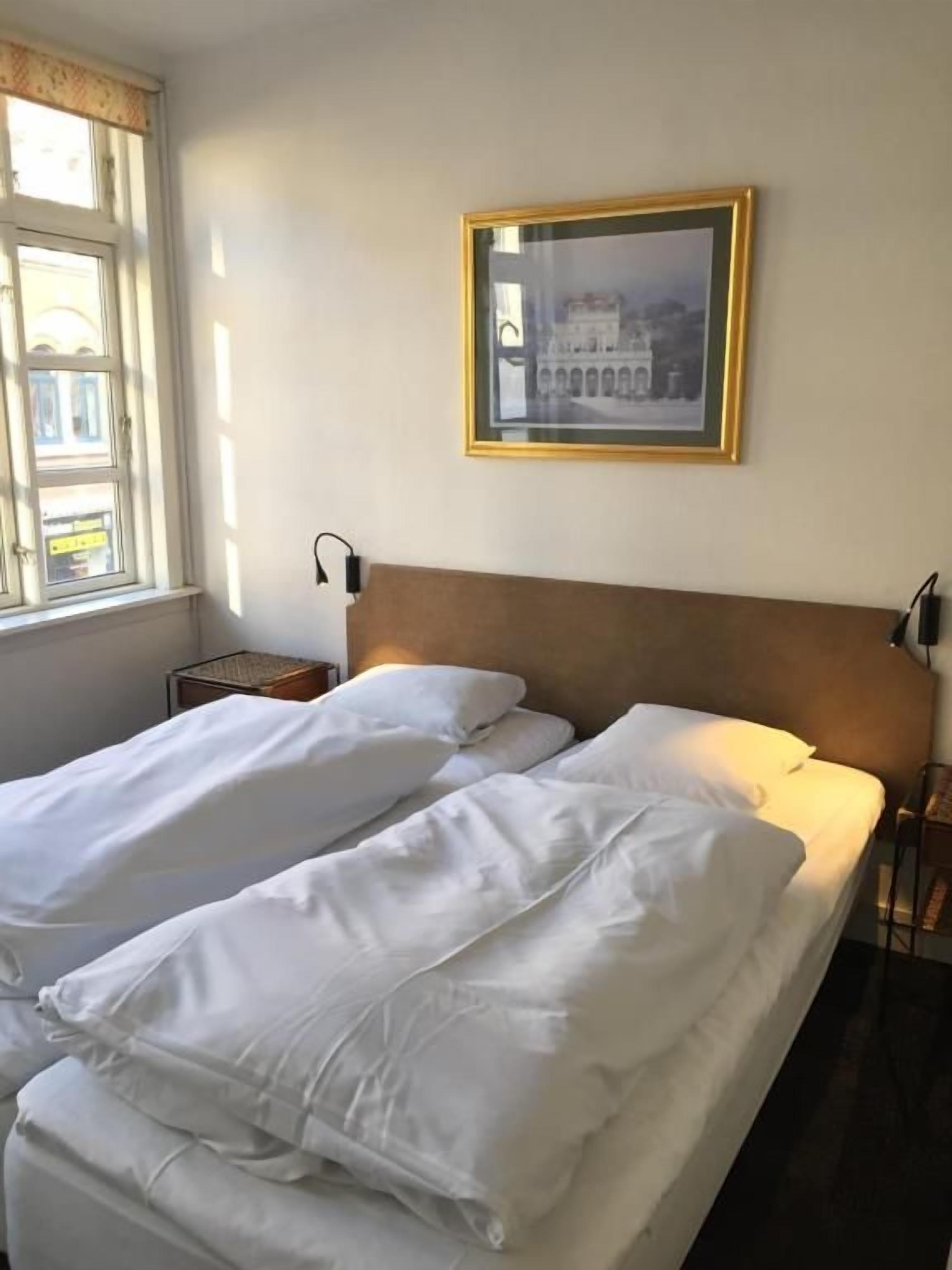 A hotel room with two beds, a framed picture on the wall, and a window with curtains.