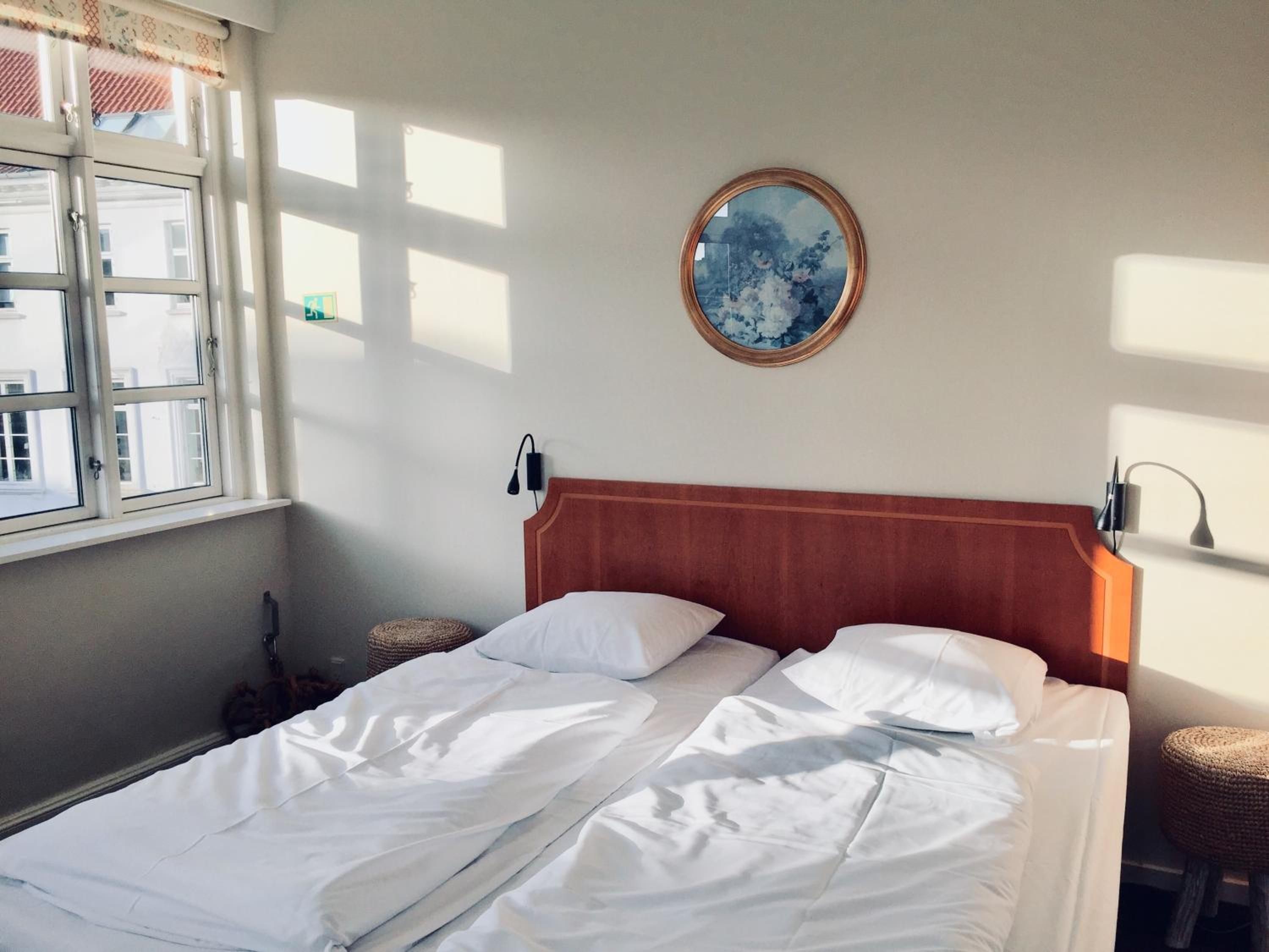 Une chambre d’hôtel avec un lit, un miroir rond accroché au mur et une fenêtre avec des rideaux.