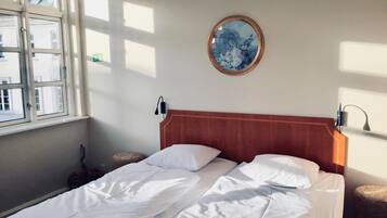 A hotel room with a bed, a round mirror on the wall, and a window with curtains.
