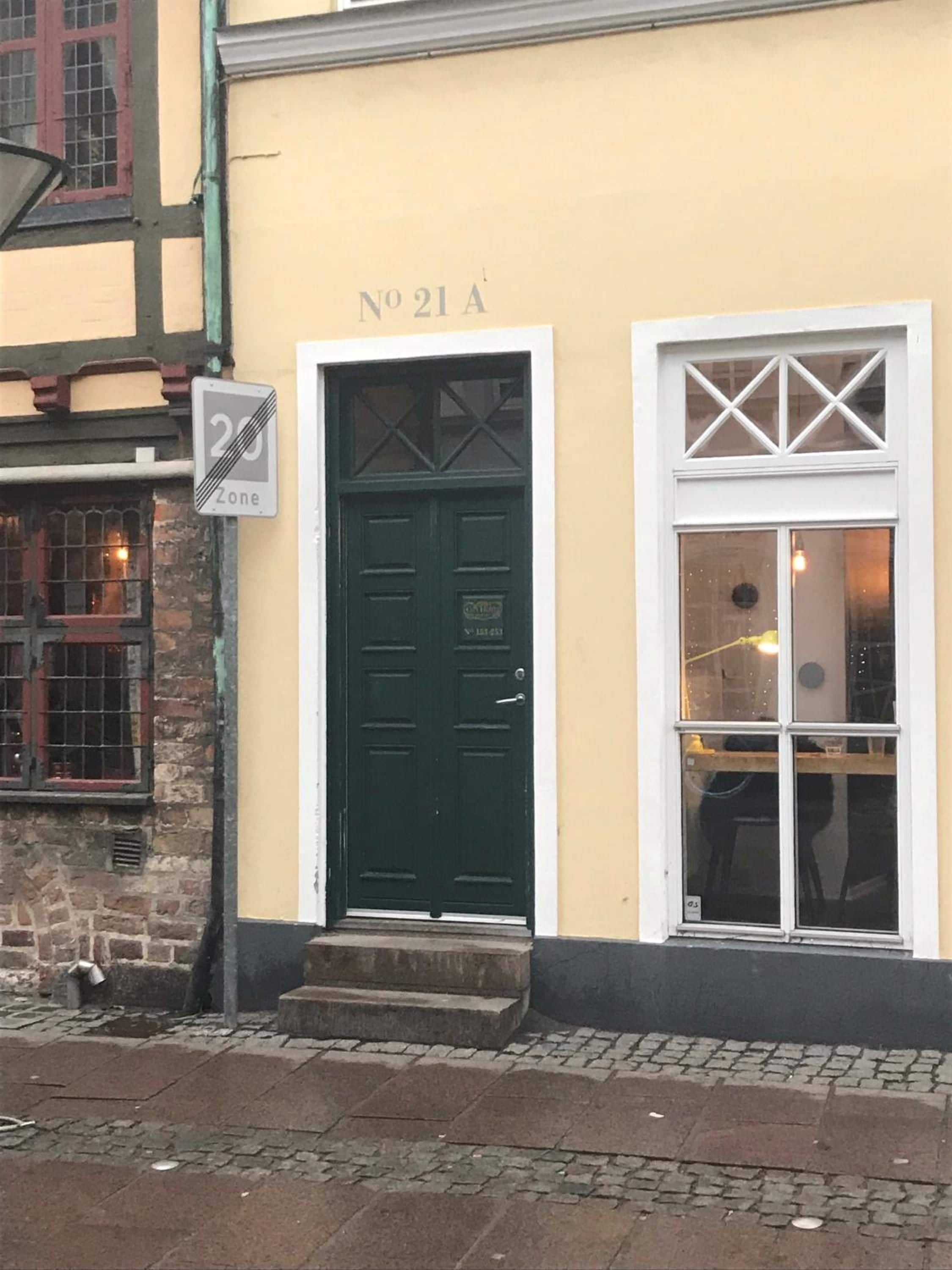 En bygning med en grøn dør og et vindue med hvid ramme. Et skilt angiver en 20-zone.