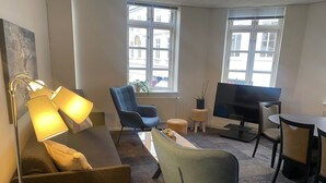 A modern living room with a sofa, armchair, TV, and dining table. - City Hotel Nattergalen Apartments (Odense)