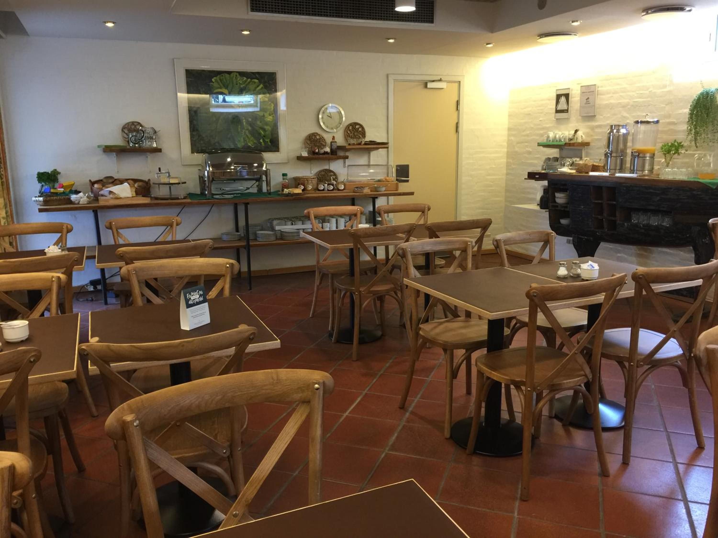 Un interior de restaurante con mesas y sillas de madera, una barra con una máquina de café y elementos decorativos en las paredes.