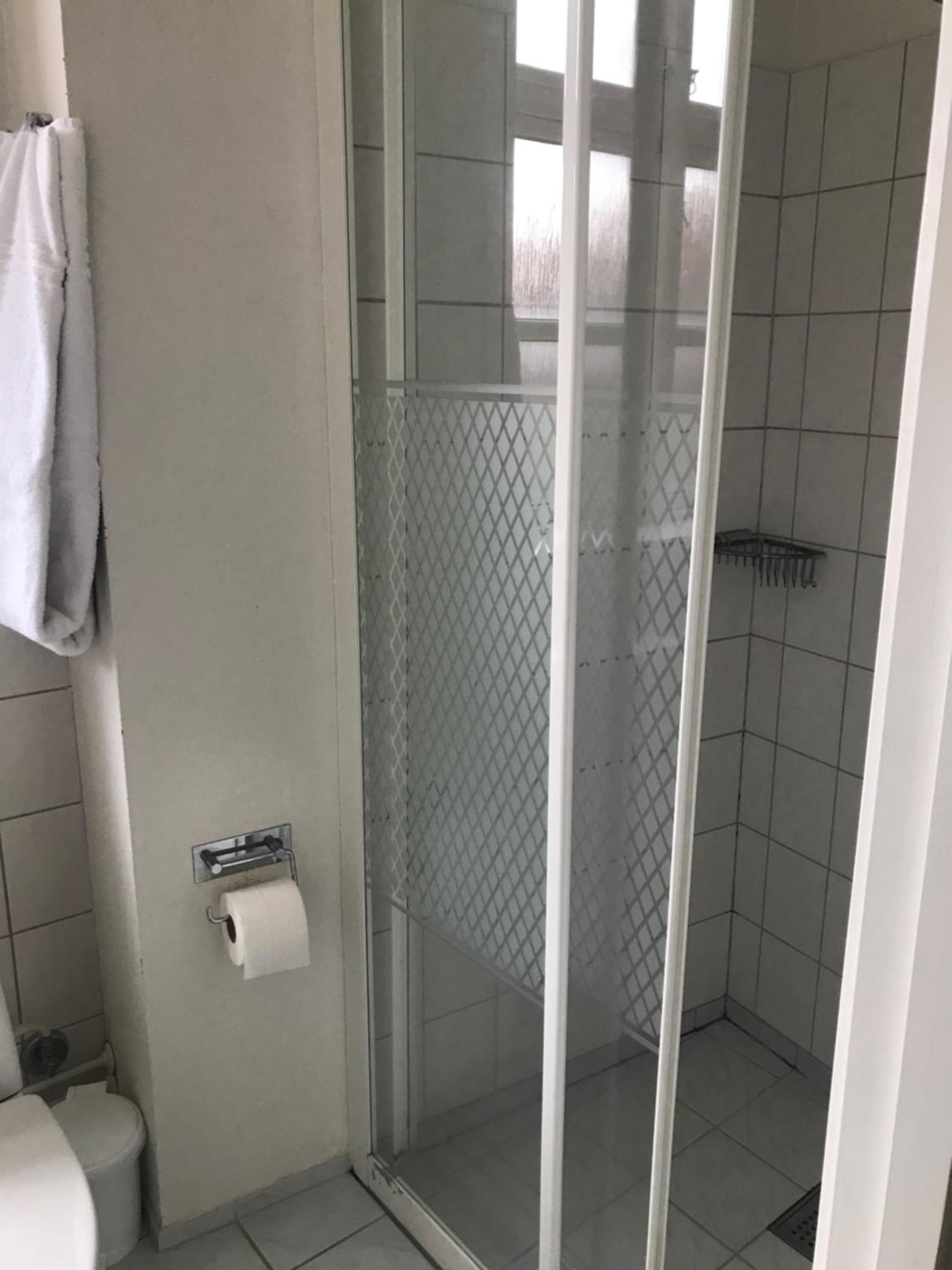 Un baño con inodoro, ducha con puerta de cristal y toalla colgada en la pared.