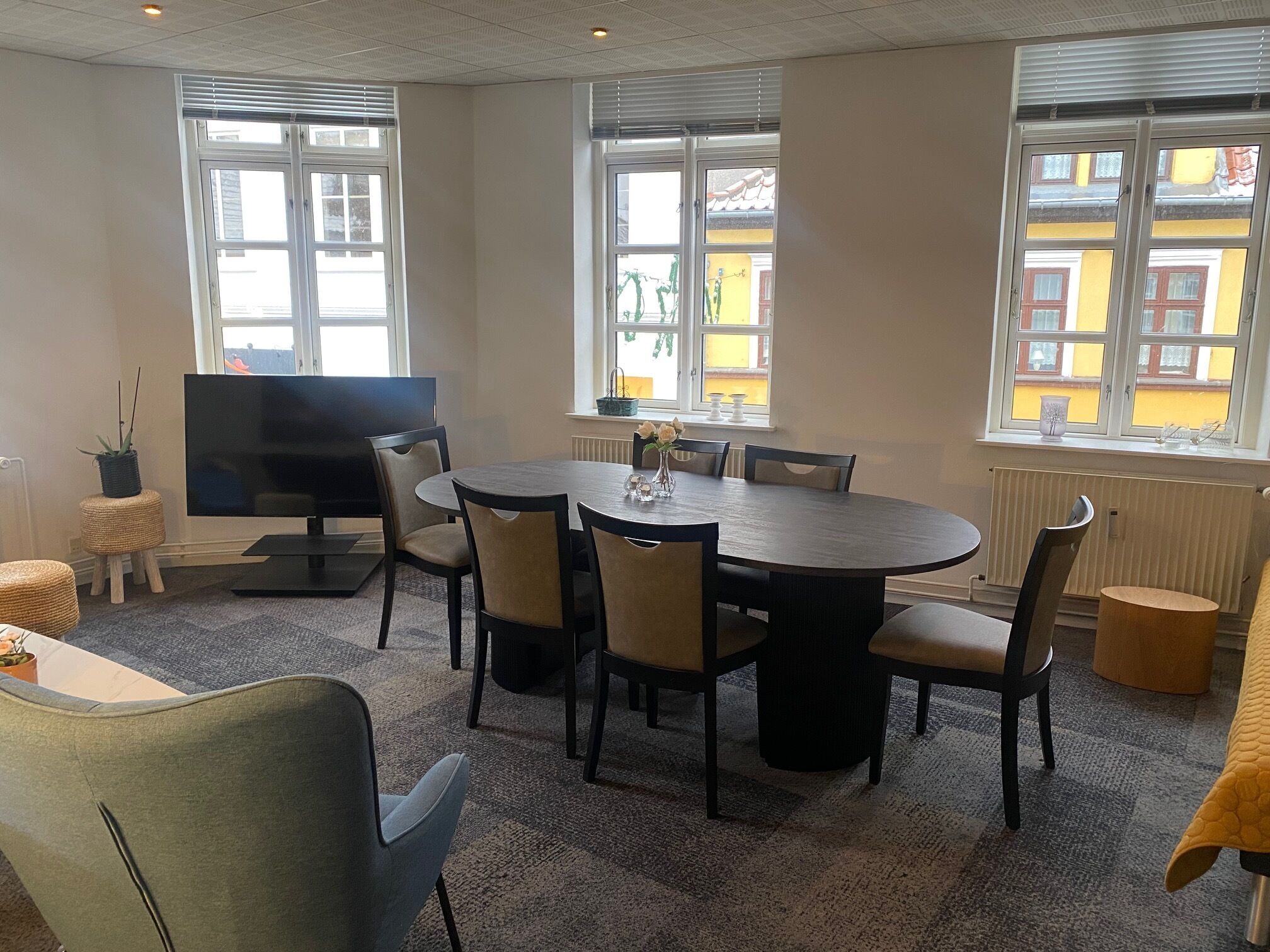 Une salle de conférence équipée d’une table ronde, de chaises, d’un téléviseur et de grandes fenêtres avec des stores.