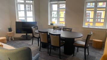 Une salle de conférence équipée d’une table ronde, de chaises, d’un téléviseur et de grandes fenêtres avec des stores.