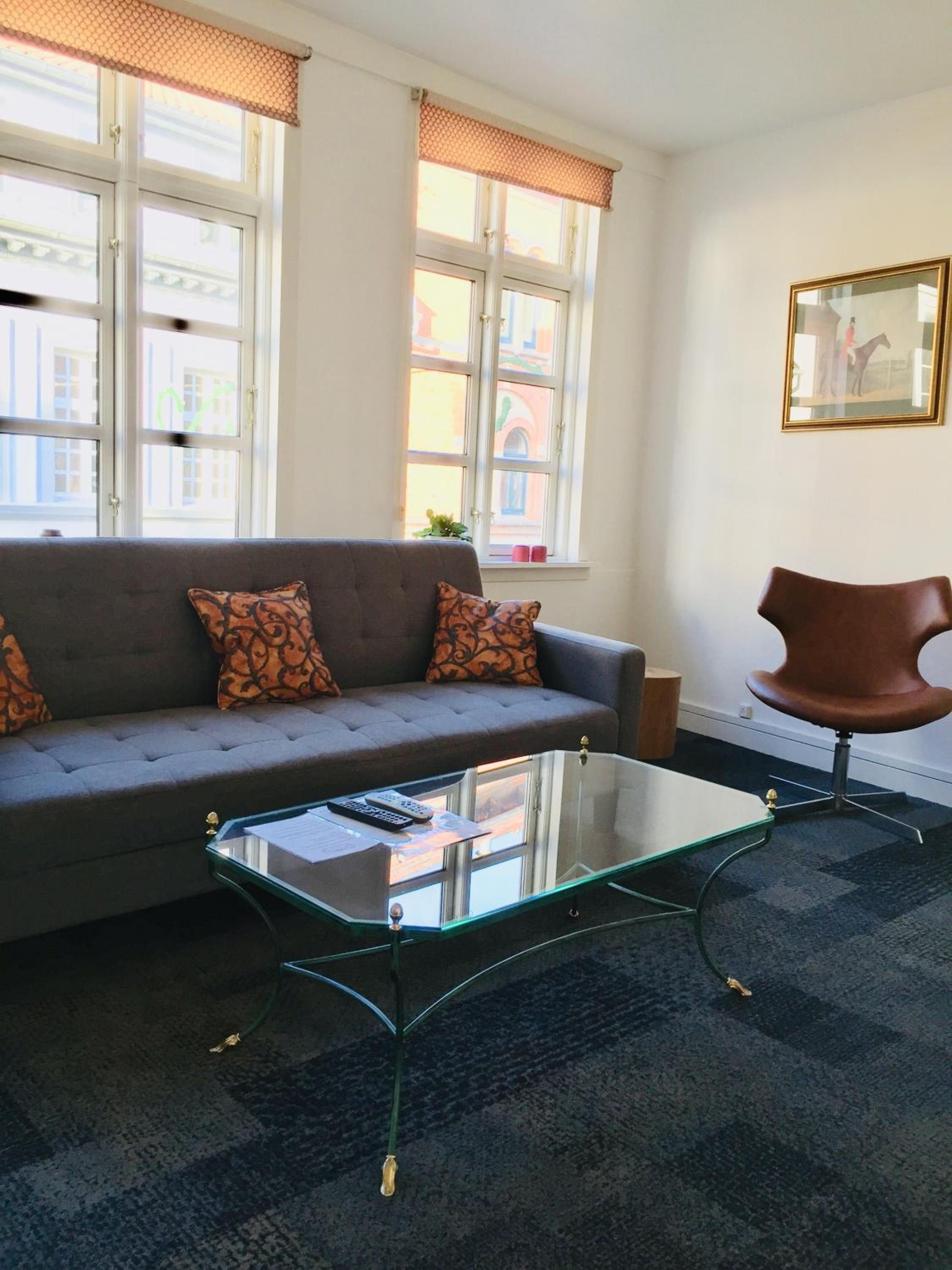 A living room with a sofa, a glass coffee table, a brown chair, and a window with a view of buildings.