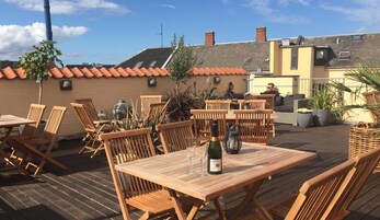 Un patio al aire libre con mesas y sillas de madera, una botella de vino y plantas en macetas.