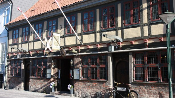 A traditional building with a red-tiled roof, multiple windows with red frames, and a bicycle parked outside. - City Hotel Nattergalen Apartments (Odense)