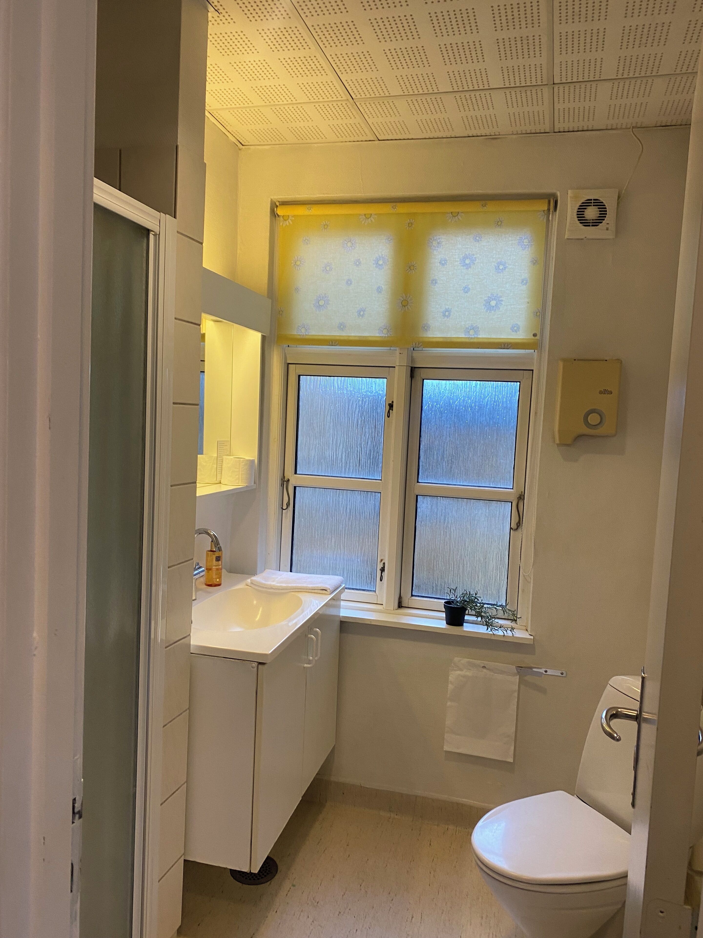 Un baño pequeño y funcional con un lavamanos blanco, un inodoro y una ventana con vidrio esmerilado.
