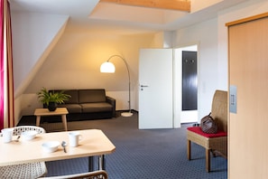A cozy room with a sofa, a table with cups and a plant, a floor lamp, and a wicker chair. - Tiemanns Boardinghouse (Lemfoerde)