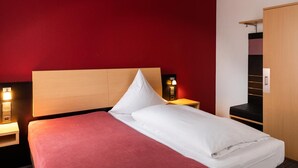 Habitación de hotel con cama, mesita de noche, armario y una lámpara de pared.