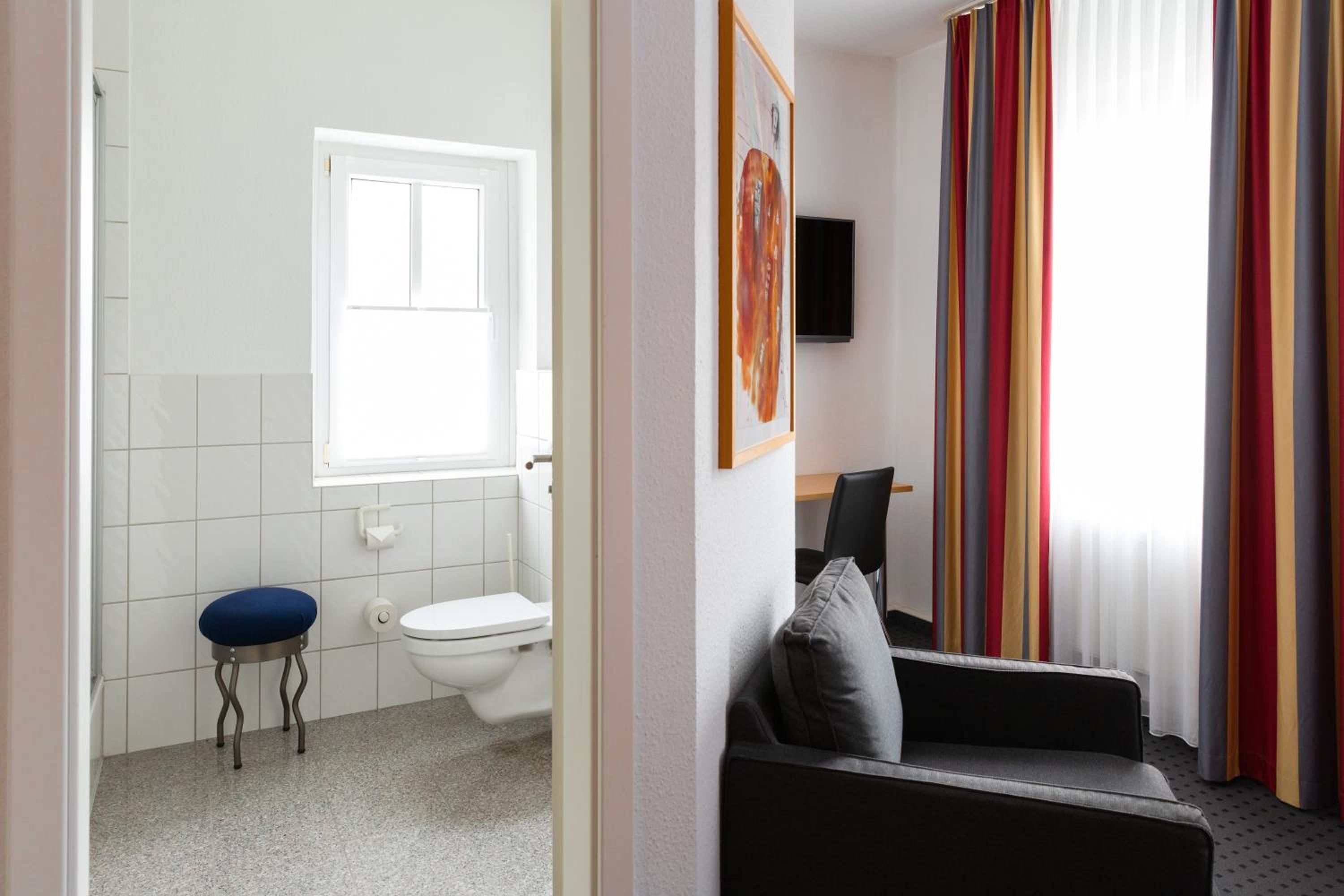 A bathroom with a toilet, a blue stool, and a window.