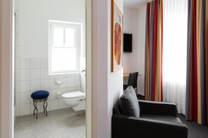 A bathroom with a toilet, a blue stool, and a window. - Tiemanns Boardinghouse (Lemfoerde)