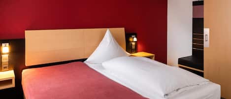 Habitación de hotel con cama, mesita de noche, armario y una lámpara de pared.