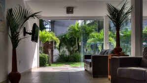 A modern living room with a glass door leading to a garden, a sofa, a coffee table, and a large potted plant. - Pousada Bahia 10 (Morro de Sao Paulo)