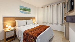 A hotel room with a bed, a nightstand, a TV mounted on the wall, and a painting of a beach scene. - Pousada Bahia 10 (Morro de Sao Paulo)